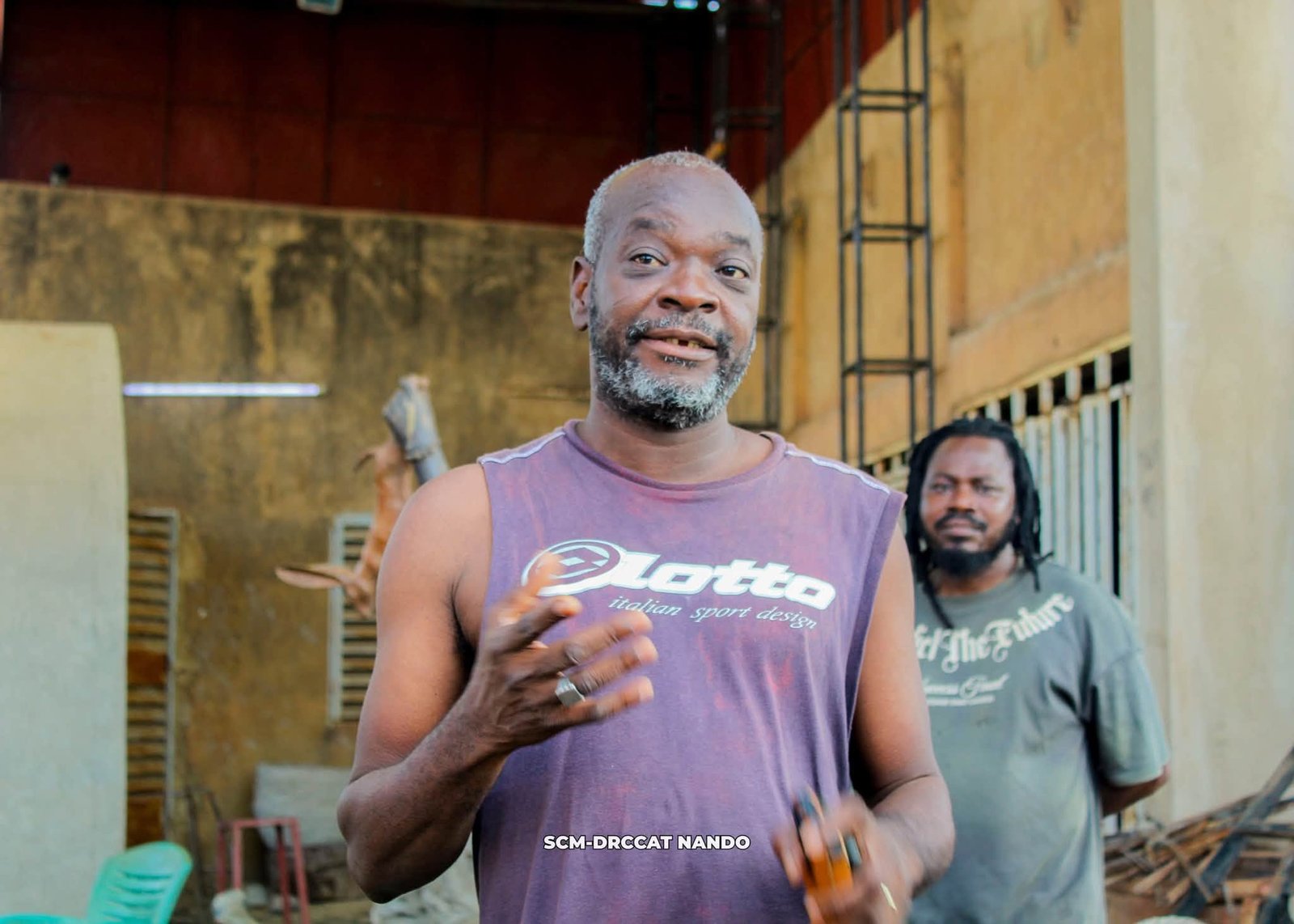 Salfo DERME, sculpteur burkinabè, devant son œuvre monumentale en bronze.